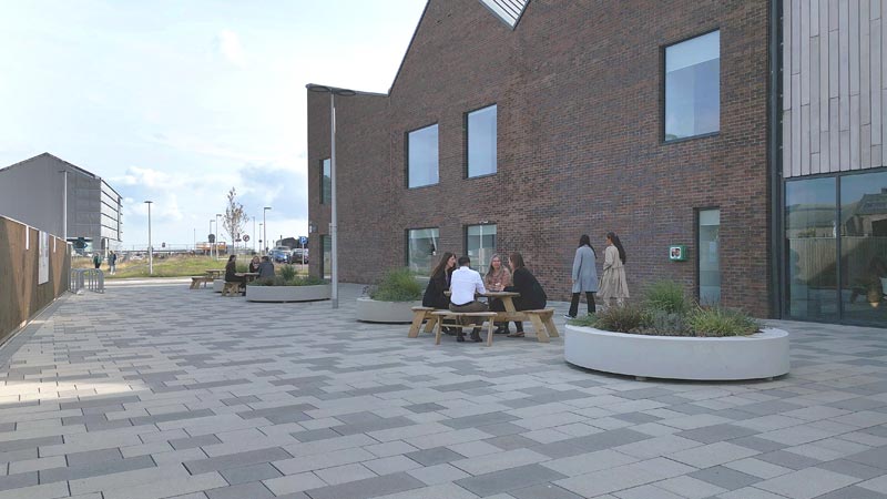 Outside Eden Campus showing the building and people chatting at an outdoor seating area.