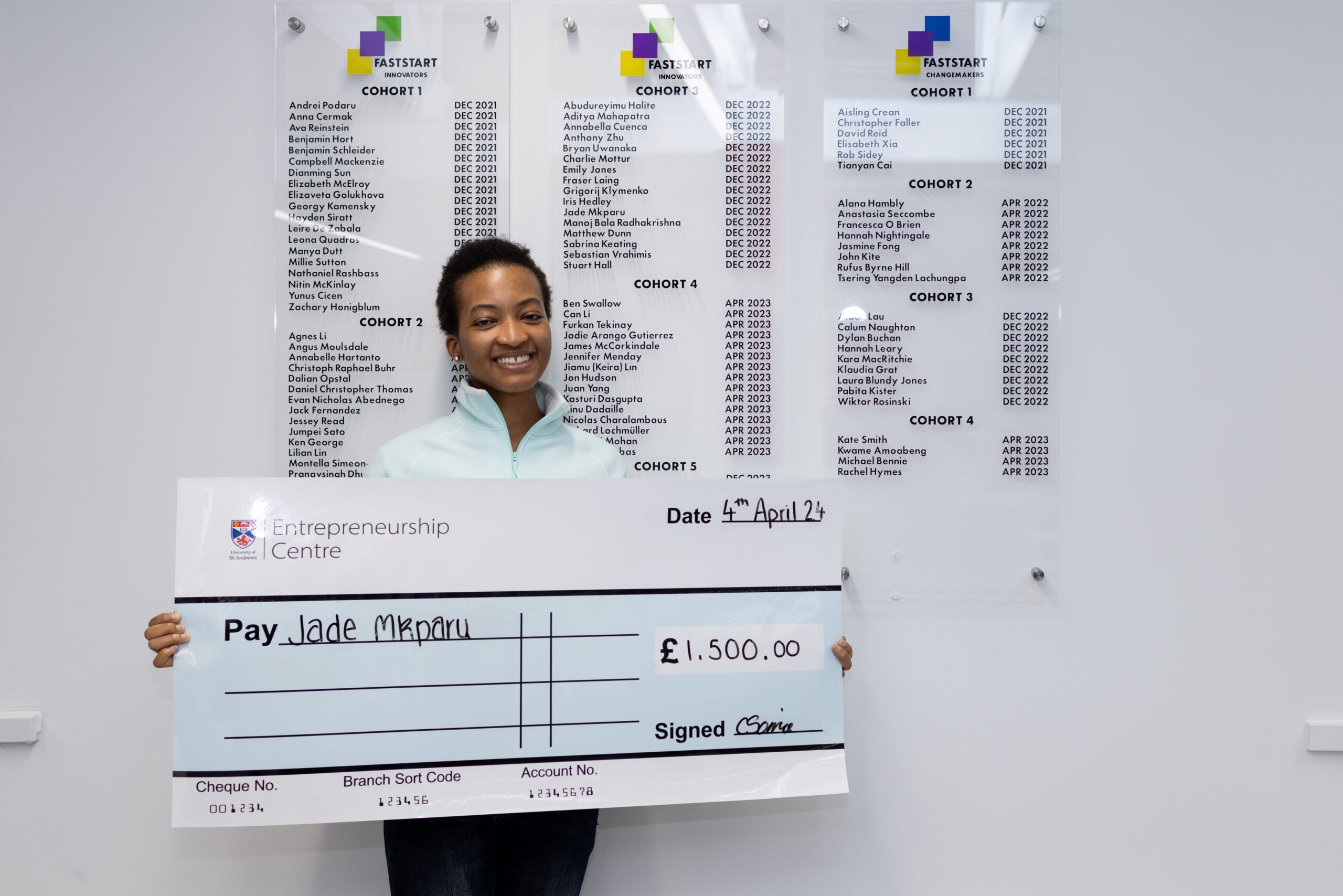 Competition winner holding cheque in front of graduation boards - Entrepreneurship Centre